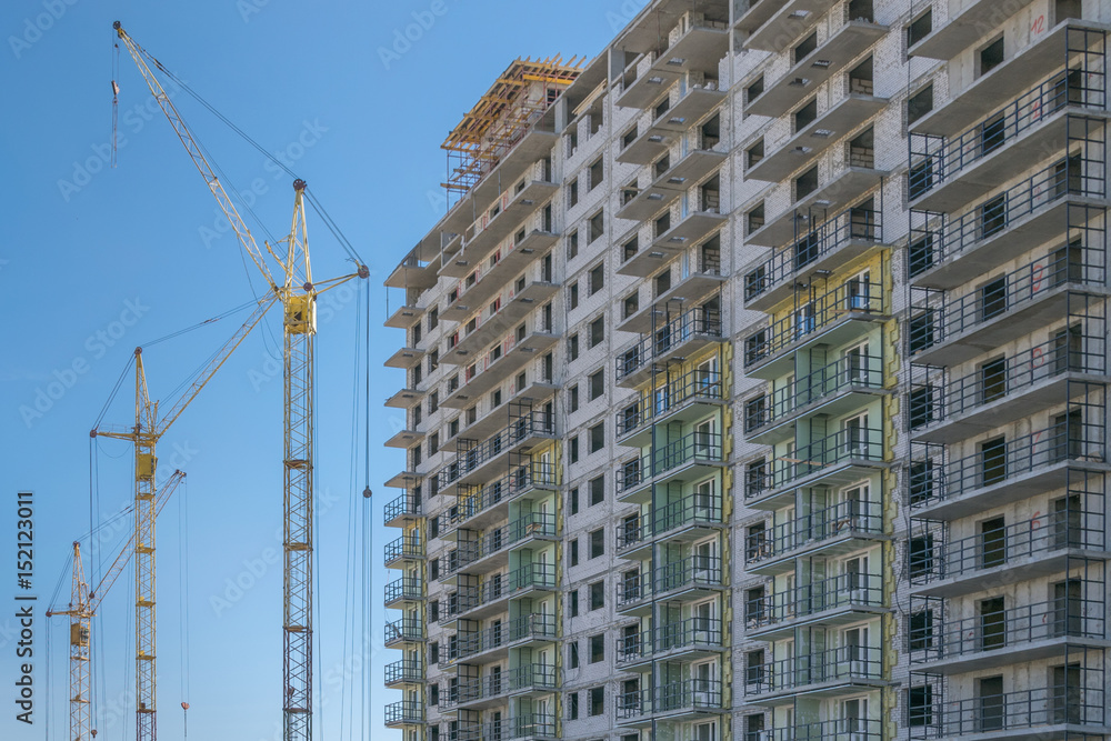 The construction site with cranes and the building against the blue sky The construction site with cranes and the building against the blue sky