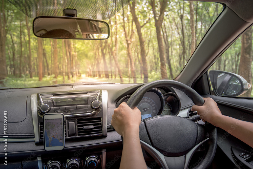 Driver's hands on the steering wheel inside of a car with beautiful road in the green forest perspective, road trip travel concepts Driver's hands on the steering wheel inside of a car with beautiful road in the green forest perspective, road trip travel concepts