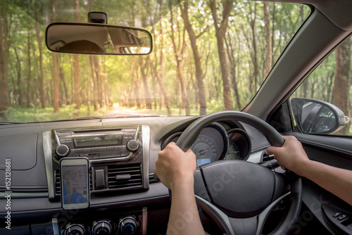 Driver's hands on the steering wheel inside of a car with beautiful road in the green forest perspective, road trip travel concepts