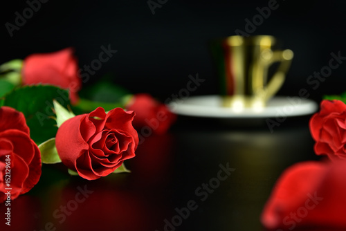 Red roses with golden cup of coffee in the evening
