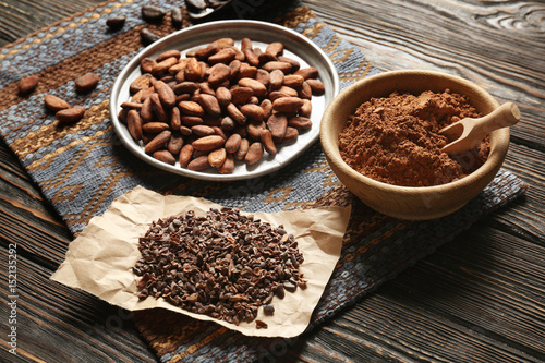 Plate with aromatic cocoa beans  powder and nibs on wooden table