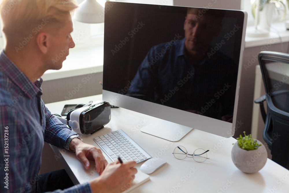 Man looking at screen and writing