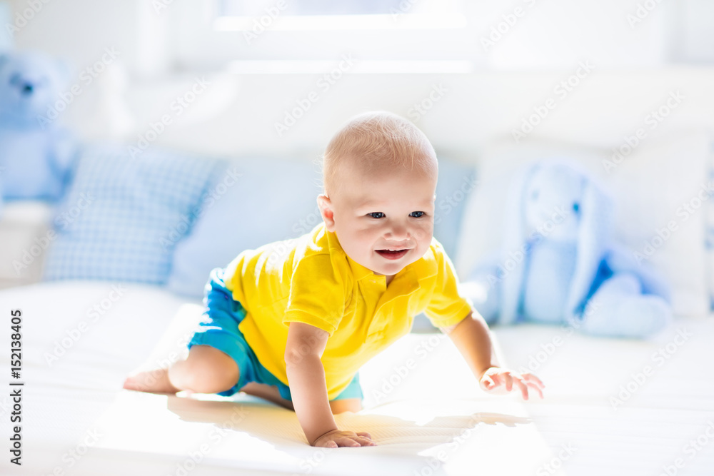 Baby boy playing on bed in sunny nursery