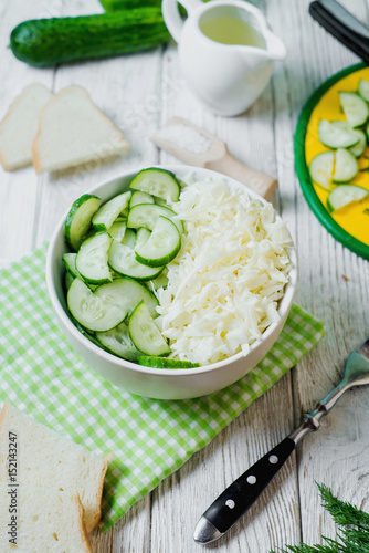  vegetarian Healthy food, light, low calorie fitness salad of fresh cucumbers, cabbage and dill with olive or sunflower oil, spices and salt on a light wooden background 