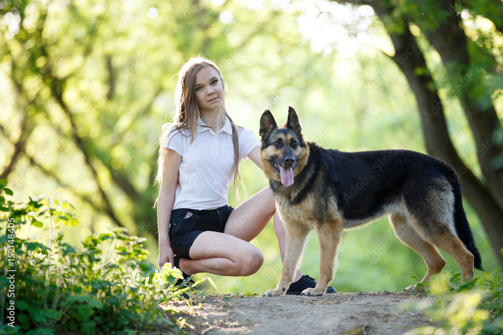 Teenage girl in white shirt with her dog sitting on pathway in the park ...