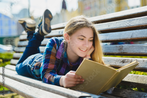 Little pretty girl reading a book and sitting on bench outdoor