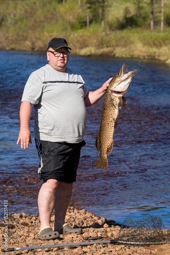 A fisherman with a big fish on the river bank