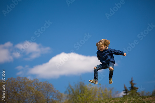 Portrait of cute happy kid boy jumping high. Child having fun and enjoying sun in the park. Lifestyle.