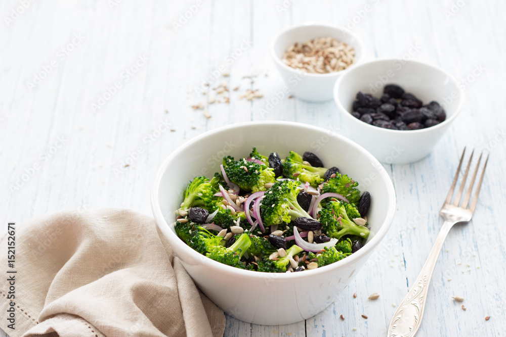 Broccoli with raisins, red onions and seeds. Healthy raw diet salad. In a white bowl on a blue wooden background. Selective focus Broccoli with raisins, red onions and seeds. Healthy raw diet salad. In a white bowl on a blue wooden background. Selective focus