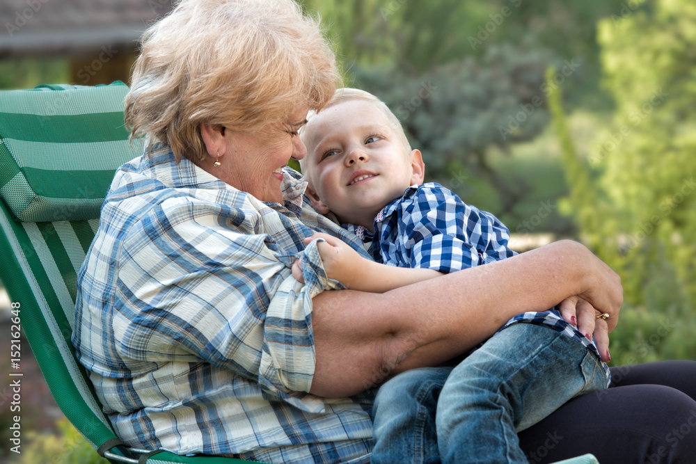 Little grandson hugging grandmother sitting in her arms.Family holiday outdoors. Little grandson hugging grandmother sitting in her arms.Family holiday outdoors.