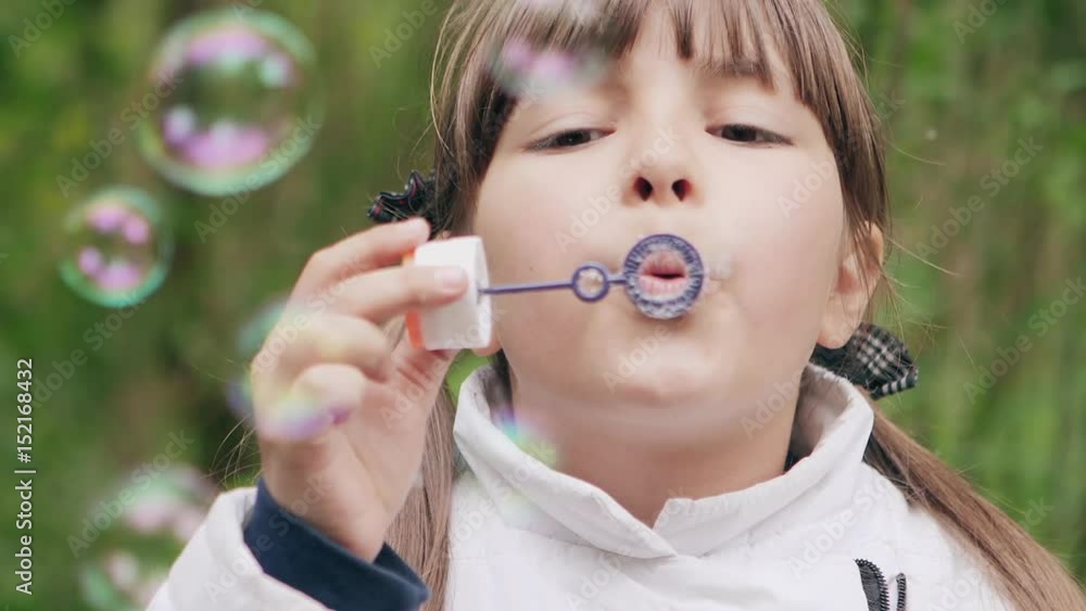 Cute little girl is blowing soap bubbles in the garden outdoors. Slow Motion 240 fps. Happy childhood concept. Closeup Cute little girl is blowing soap bubbles in the garden outdoors. Slow Motion 240 fps. Happy childhood concept. Closeup