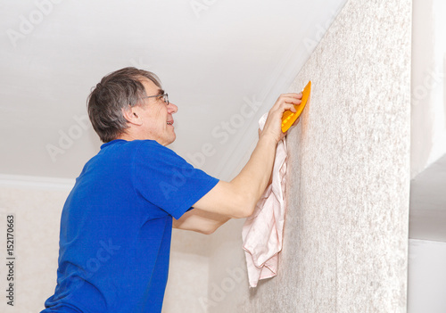 man smoothes the wallpaper with a spatula