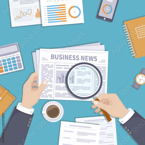 Man reading latest business news. Magnifying glass over newspaper. Businessman holding in his hand journal on the desktop. Coffee break in the workplace. Documents, notebook, coffee. View from above.
