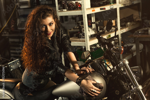 Gorgeous young woman polishing her motorbike at the workshop