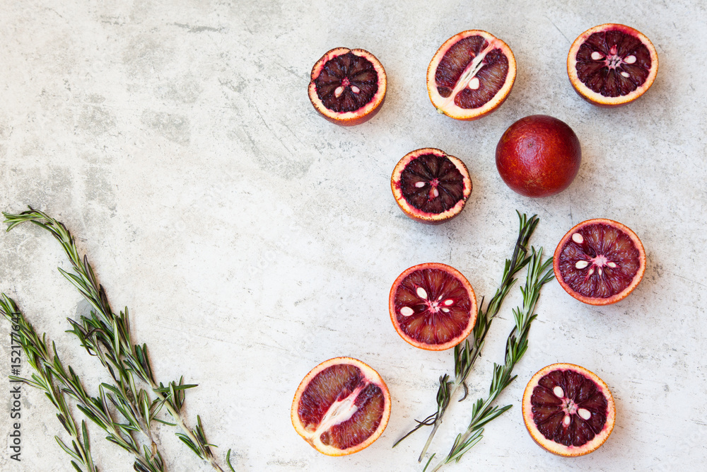 Red Sicilian orange whole and cut on a light background with branches of rosemary. Daylight, open space for your text.