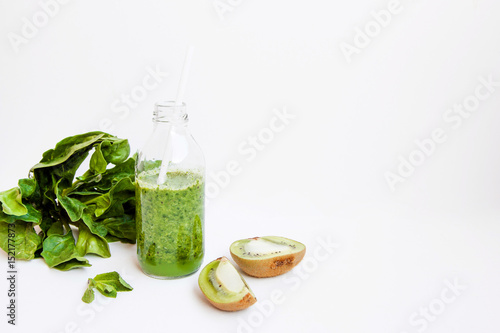 Green cocktail in a bottle and in a glass with spinach, mint, rosemary, kiwi and apple on a light background.