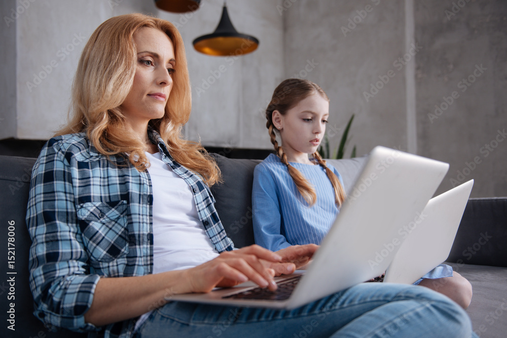 Attractive mature parent and little daughter using laptops indoors Attractive mature parent and little daughter using laptops indoors