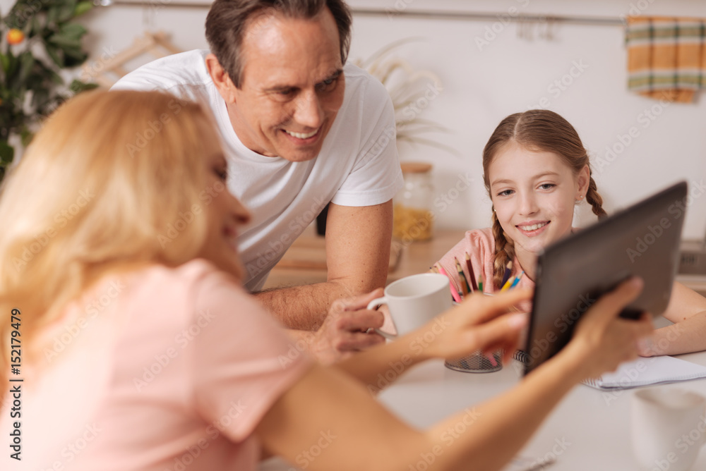 Amused mother enjoying new gadget with family at home Amused mother enjoying new gadget with family at home