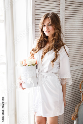 Beautiful sexy girl in a dress and lingerie posing in the morning in the interior, the room, the light room