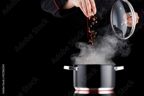 Принти на полотні Modern chef in professional uniform adding spice to steaming pot