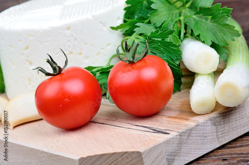 Cheese with tomatoes, green onion and parsley on chopping wooden