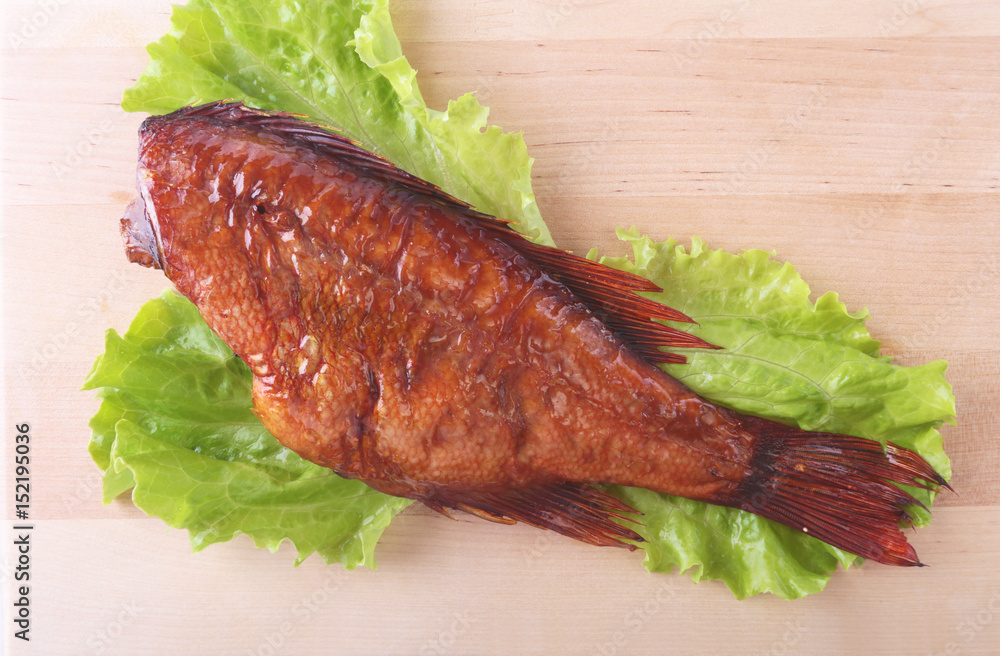 Smoked fish and lemon on green lettuce leaves on Wooden cutting board isolated on white background. Smoked fish and lemon on green lettuce leaves on Wooden cutting board isolated on white background.