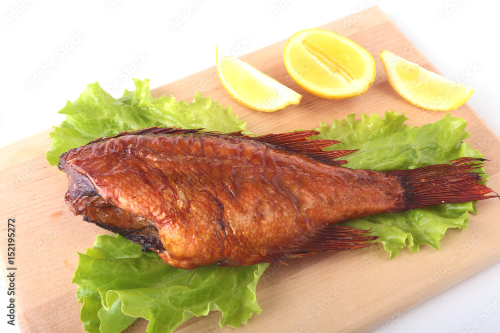 Smoked fish and lemon on green lettuce leaves on Wooden cutting board isolated on white background.