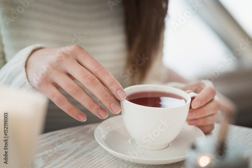 Female hands holding a white cup of tea standing on the table top view