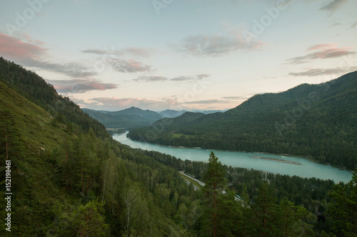 The river flows between the mountains covered with forest on the Altai at sunset