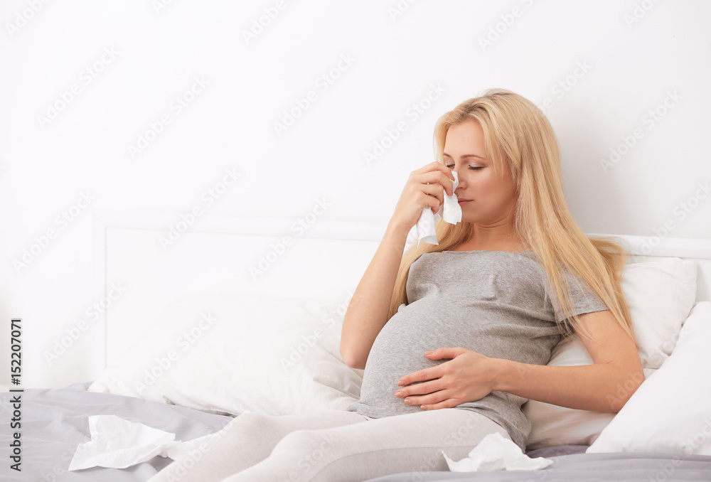 Pregnant woman with allergy sitting on bed at home Pregnant woman with allergy sitting on bed at home