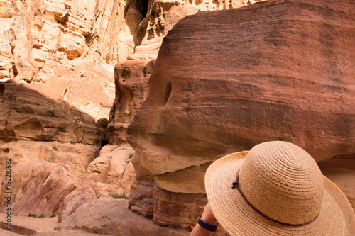 Woman wearing a straw hat looking up at the colorful sandstone in Al-Siq, Petra Jordan. The woman is in the lower right corner of the photo and her hat blends in with the color of the stone.