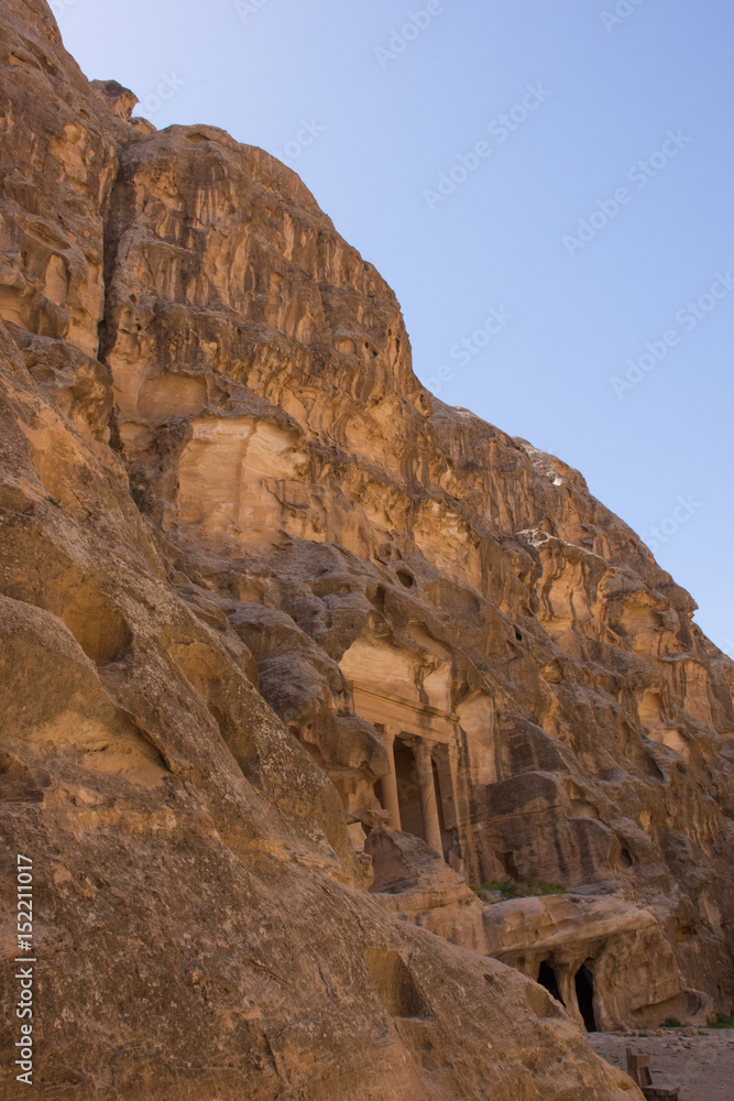 The distant ancient carved sandstone columns of Siq al Barid, Little Petra, Jordan. Buildings are formed from caves and have cisterns for water collection. Photographed from below.