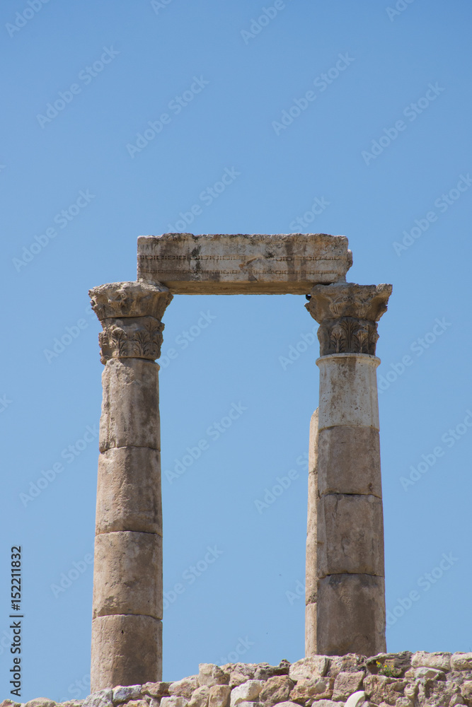 Close up of columns of ancient Roman Temple of Hercules with stone beam or lintel on carved capitals at the Citadel against a deep blue cloudless sky.