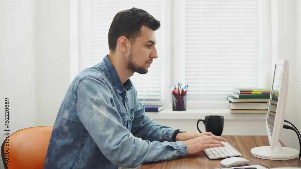 Young businessman working on computer in stylish modern office. Computer, phone and cup on the table. Shot in 4k Young businessman working on computer in stylish modern office. Computer, phone and cup on the table. Shot in 4k
