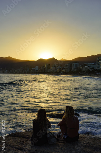 Girls on the stone looking at the sea during sunset on Ipanema beach, Rio de Janeiro with Twoo Brothers hill and Gavea Stone in background © Fred Pinheiro