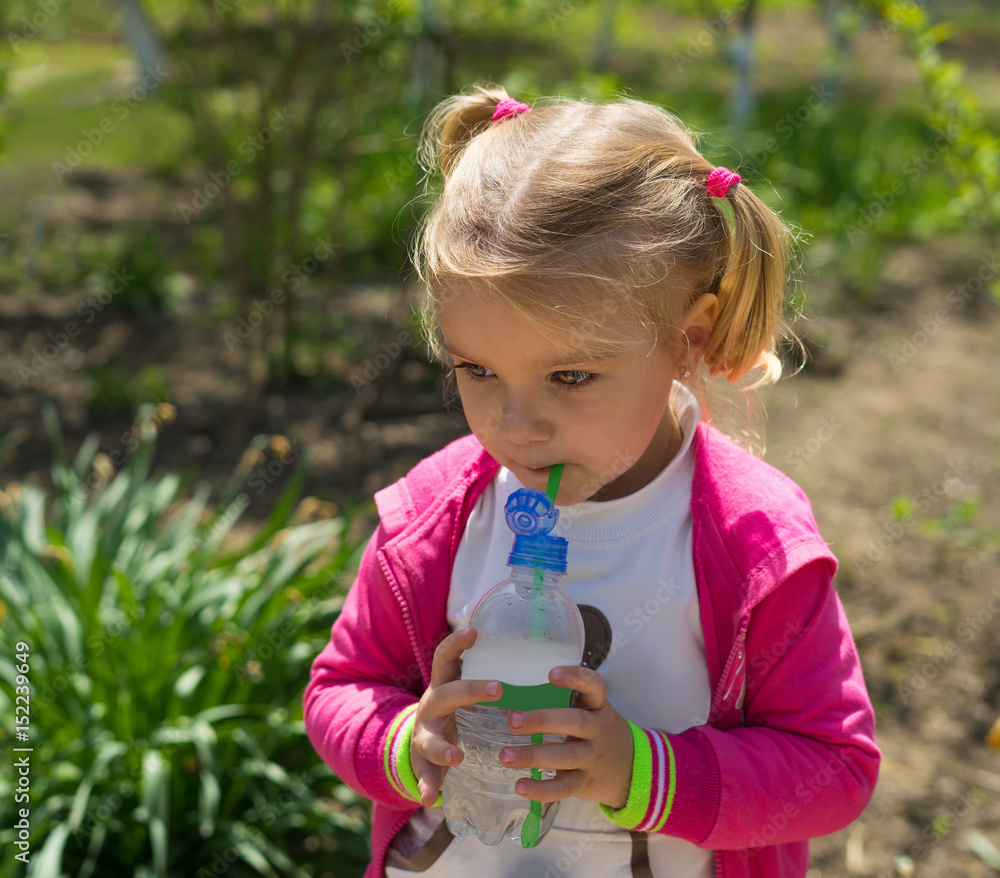 Small cute girl drinking water from plastic bottle. Green sunny photo