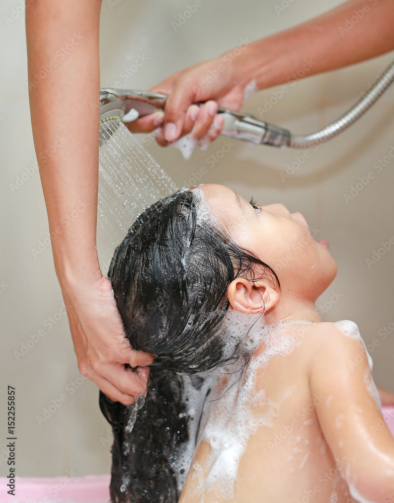 Naklejka premium Little girl bathing and washing hair in bubble bath.