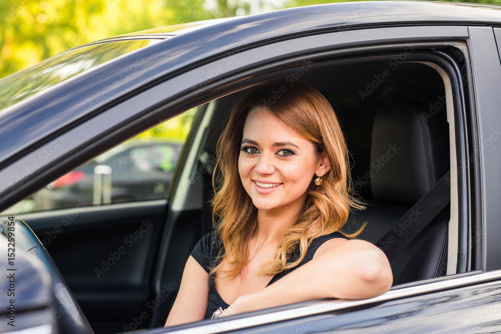 Smiling young pretty woman with black car. Concept of travel, rent car or buying car.