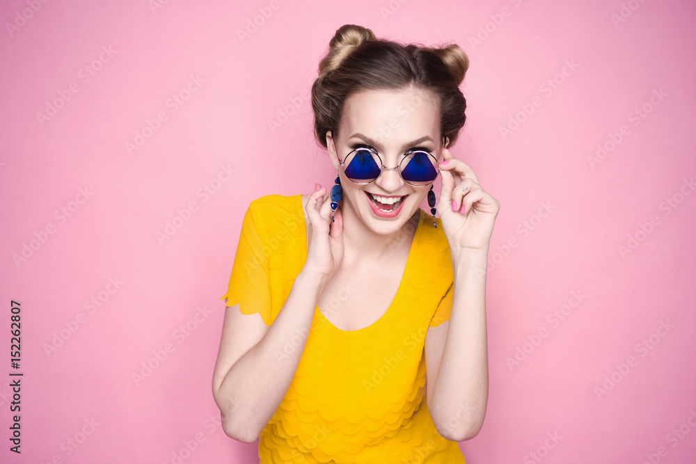 close-up portrait of a beautiful young blonde girl in fashionable sunglasses on a pink background in the studio in a yellow blouse and jeans holding a popular phone smiling close-up portrait of a beautiful young blonde girl in fashionable sunglasses on a pink background in the studio in a yellow blouse and jeans holding a popular phone smiling