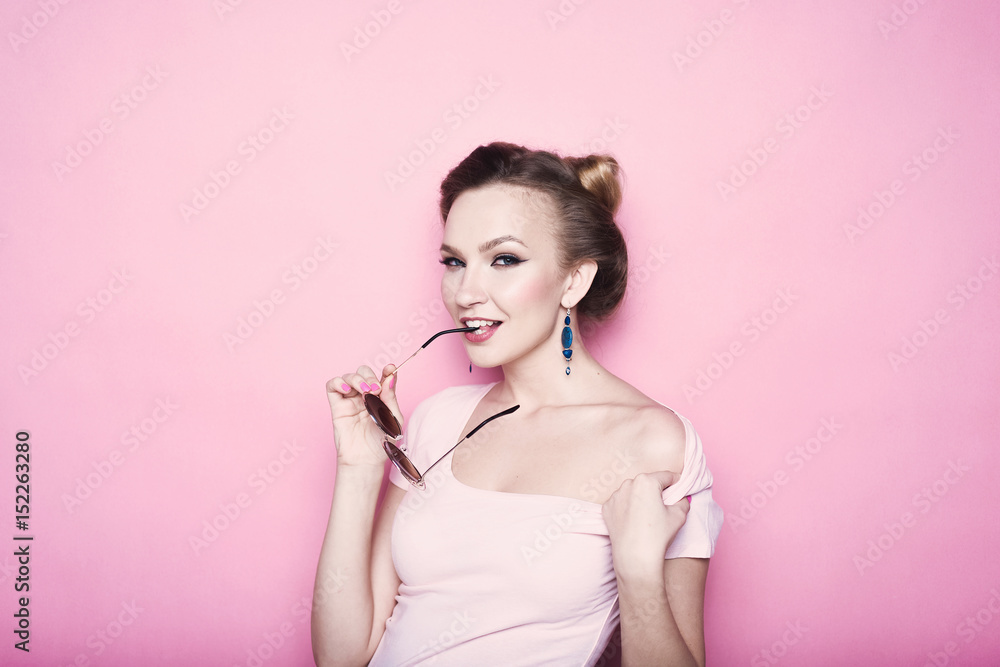 close-up portrait of young beautiful slim sexy young blonde woman in a retro pin-up style on pink background in studio wearing sunglasses smiling and posing close-up portrait of young beautiful slim sexy young blonde woman in a retro pin-up style on pink background in studio wearing sunglasses smiling and posing