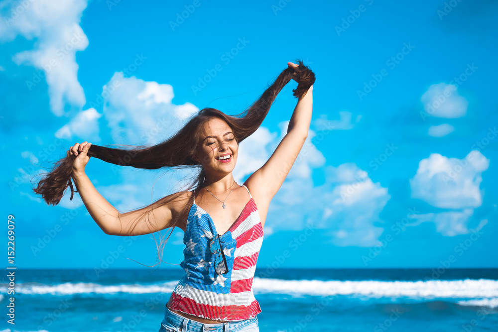 close-up portrait of a beautiful young brunette girl with long hair on a background of blue sea with waves and sky with clouds on a sunny day, lifestyle, posing and smiling, wind close-up portrait of a beautiful young brunette girl with long hair on a background of blue sea with waves and sky with clouds on a sunny day, lifestyle, posing and smiling, wind