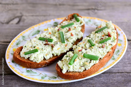 Guacamole toast on a plate and a vintage wooden background. Open rye sandwiches with guacamole, fresh green onion and spices. Homemade vegan toast recipe. Closeup