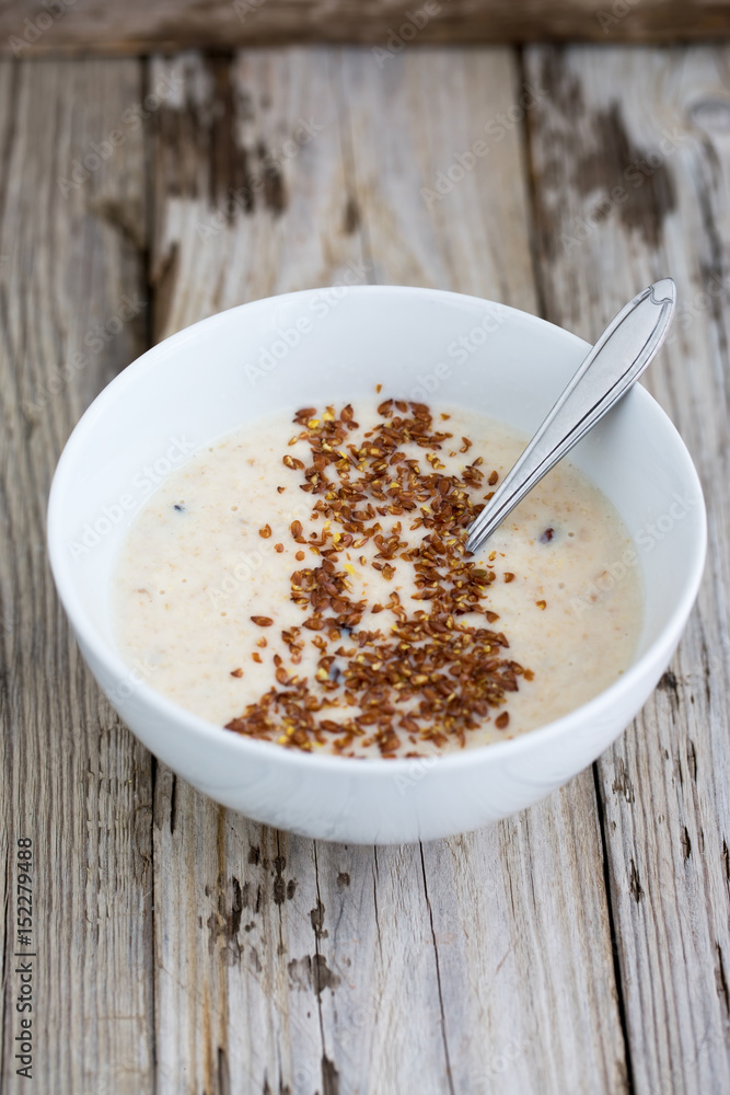 Fresh cooked oatmeal porridge with crushed linseed. On wooden table. Natural light, selective focus. Fresh cooked oatmeal porridge with crushed linseed. On wooden table. Natural light, selective focus.