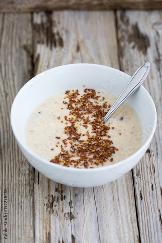 Fresh cooked oatmeal porridge with crushed linseed. On wooden table. Natural light, selective focus. 