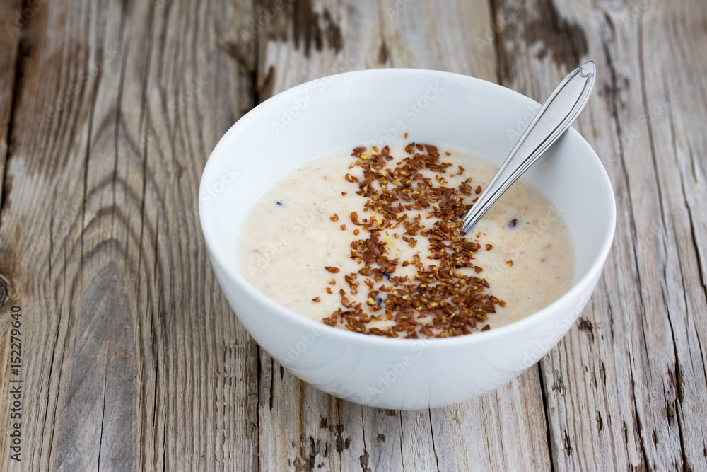 Fresh cooked oatmeal porridge with crushed linseed. On wooden table. Natural light, selective focus. Fresh cooked oatmeal porridge with crushed linseed. On wooden table. Natural light, selective focus.