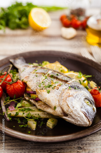 Baked whole fish, served with roasted vegetables and lemon.