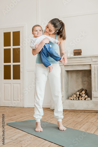 Mother holding baby boy on her arms and ready to yoga practice at home