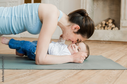 Smiling mother doing plank exercise with her son on yoga mat