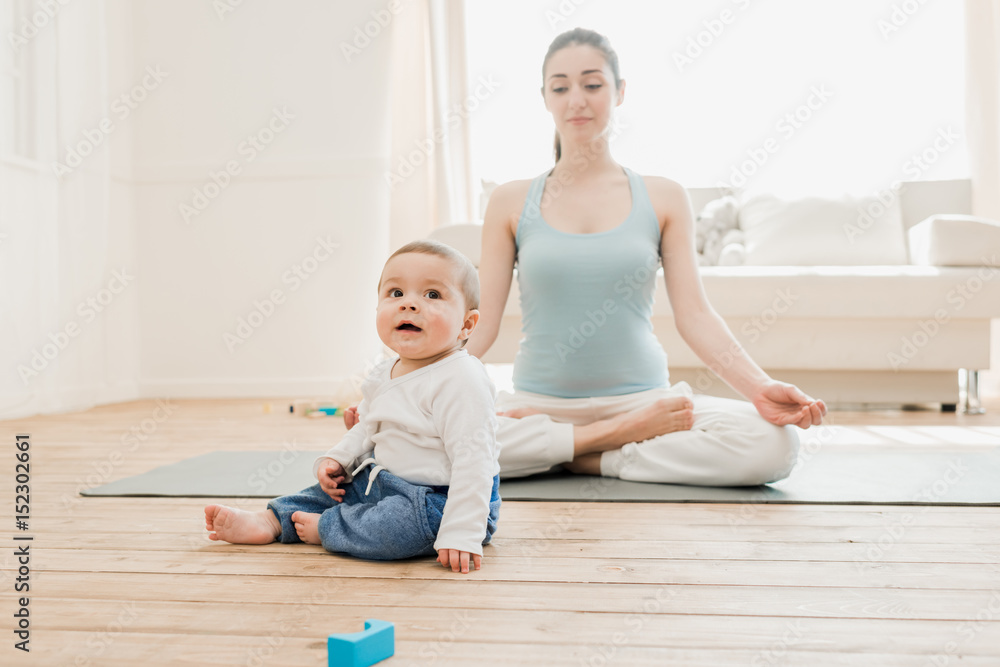 Baby boy playing with toys while his mother meditating at lotus position. Baby boy playing with toys while his mother meditating at lotus position.