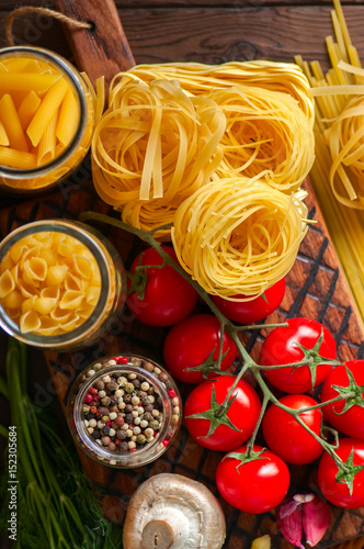 Assortment of raw types and shapes of italian pasta and wooden board on a black slate background. Close up. Top view and copy space.
